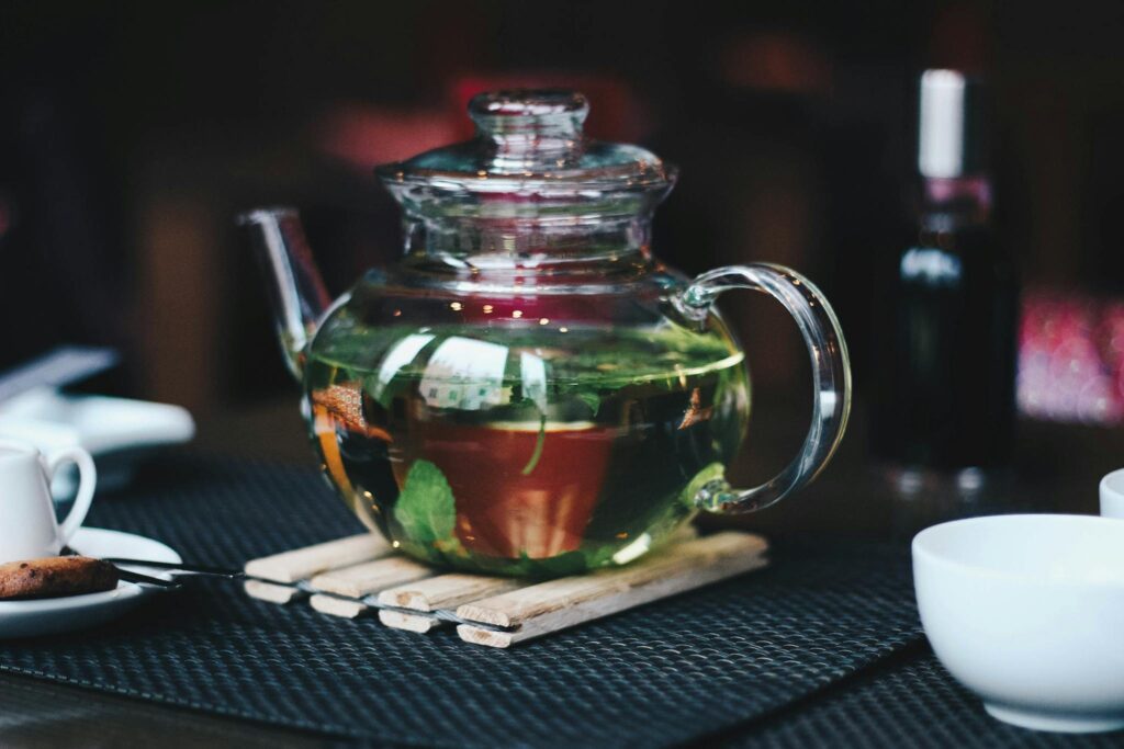 A glass teapot with herbal tea, surrounded by cups and a cookie, creating a cozy atmosphere.