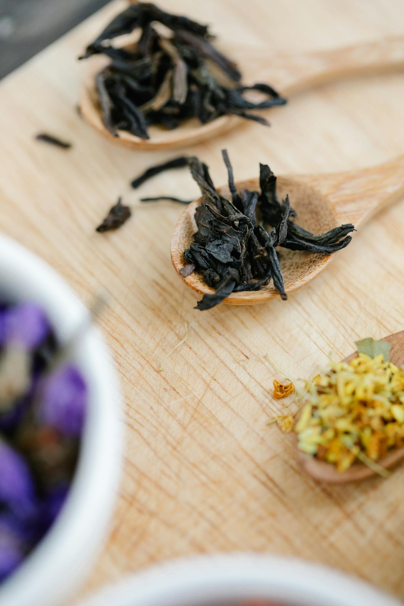 Close-up of dried herbs and flowers on wooden spoons, perfect for culinary and aromatic uses.